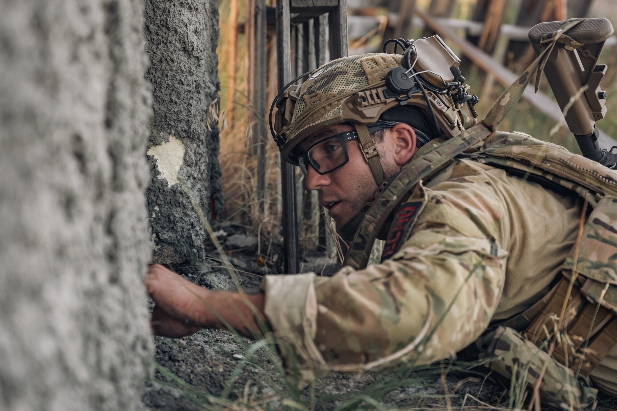 An Airman in a prone position reaches through doorway.