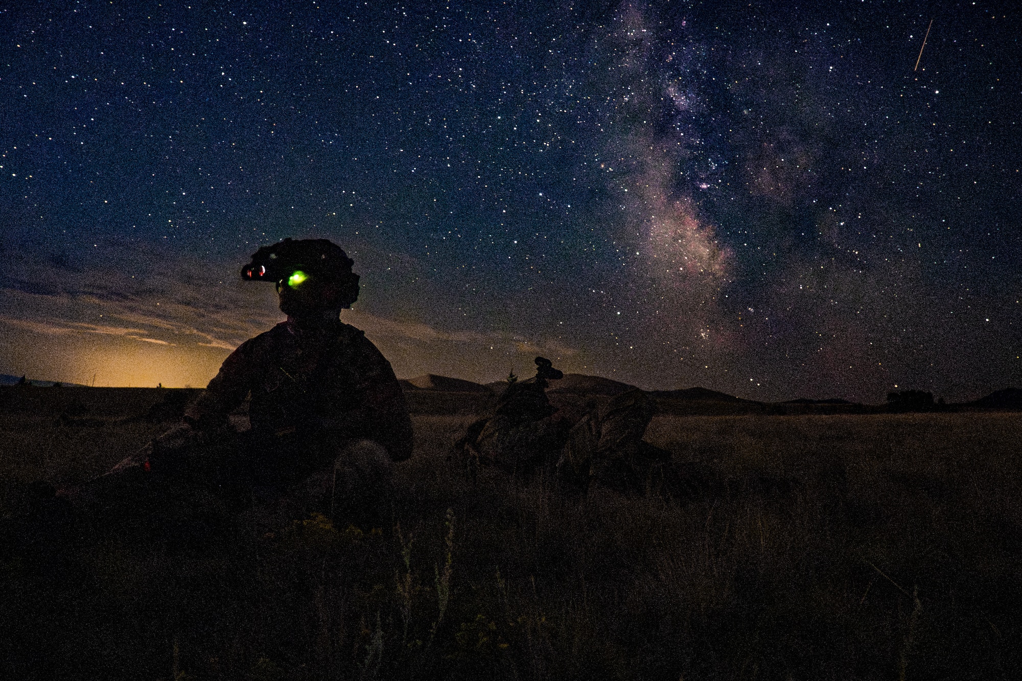 A silhouette of an Airman siting in a field with stars in the background.