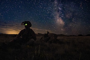 A silhouette of an Airman siting in a field with stars in the background.