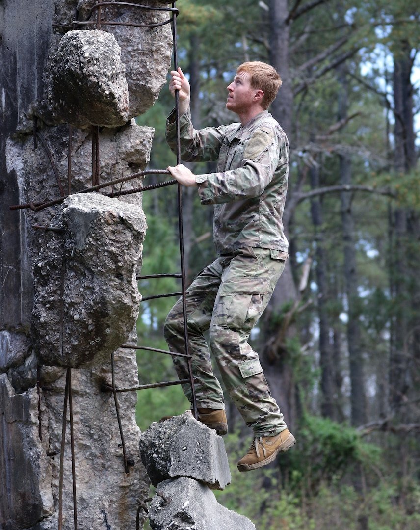 Uniformed service member climbing obstacle outdoors