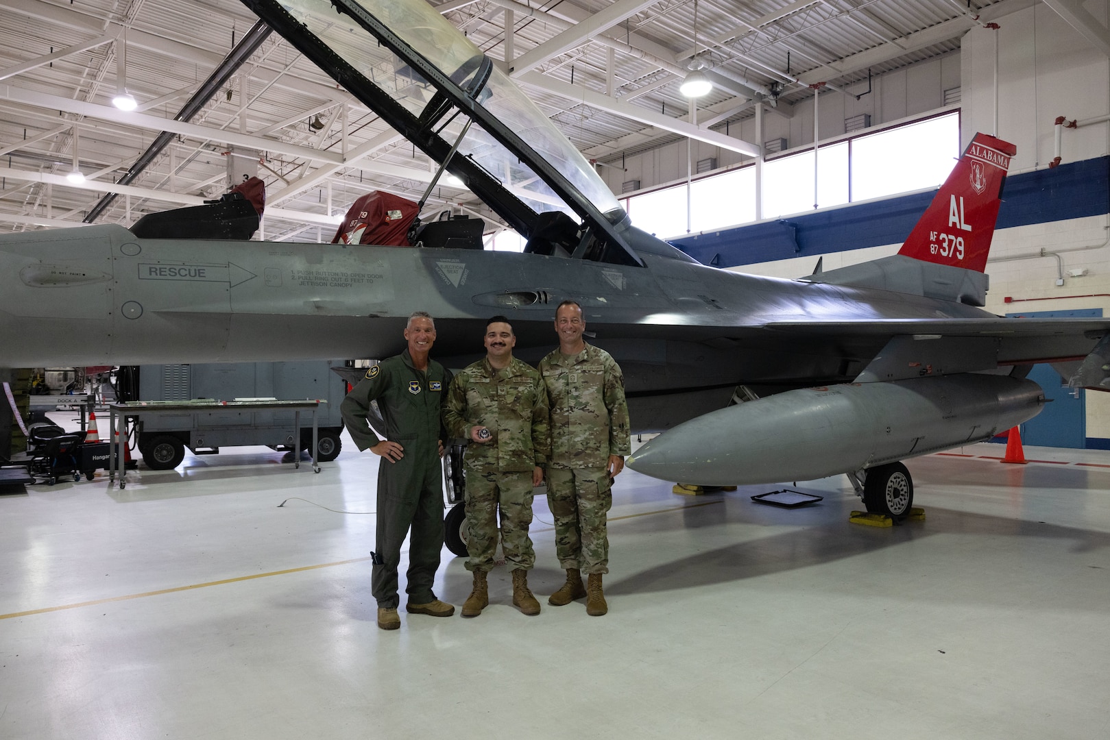 From left, U.S. Air Force Maj. Gen. Gregory Kreuder, commander, 19th Air Force, Tech. Sgt. Andrew Quiroz, 162nd Aircraft Maintenance Squadron avionics technician, and Chief Master Sgt. Keith Scott, command chief 19th Air Force, gather for a photo  at Morris Air National Guard Base, Ariz., Aug. 19, 2025. Quiroz was recognized for his contributions to the maintenance of Aircraft 379. Aircraft 379, critical for student pilot training, underwent depot-level maintenance, averting a year long wait and saving millions of dollars. This initiative exemplifies the 162nd Wing’s commitment to efficient resource management in support of the 19th Air Force mission to produce the next generation of aviators. (U.S. Air National Guard photo by Staff Sgt. Guadalupe Beltran)
