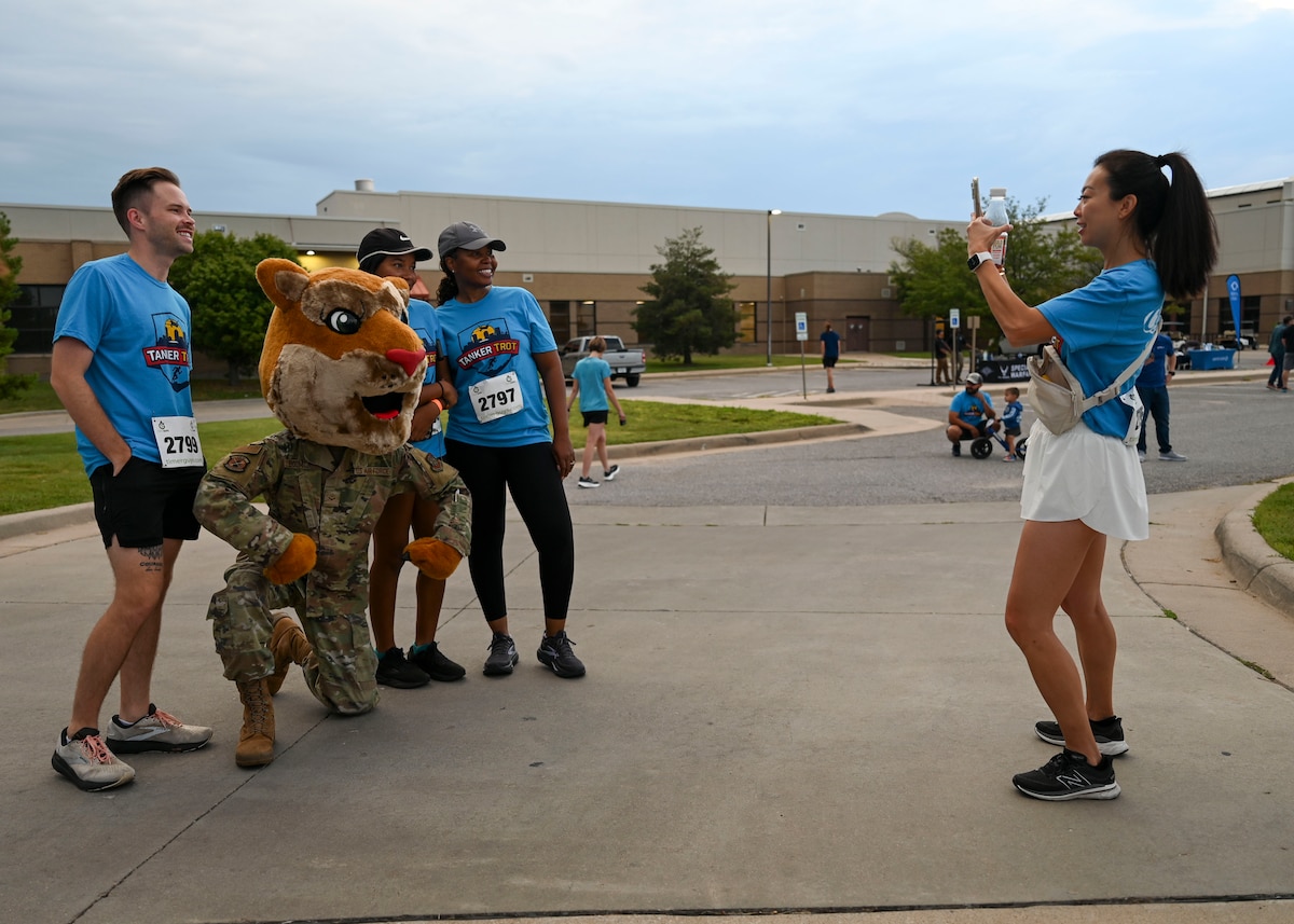 A woman takes a photo of people with a person dressed in a military uniform with a cat cask on.