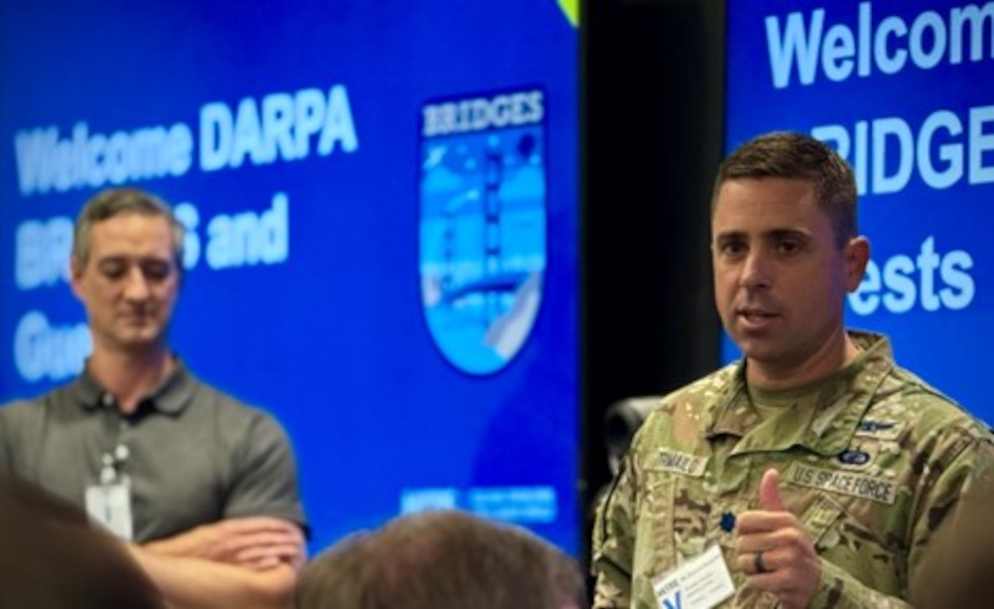 U.S. Space Force Col. Tim Trimailo, director of Space Systems Command’s Commercial Space Office (COMSO), addresses a group of industry leaders at the final meeting of the BRIDGES Consortium July 24, 2025, as Tim Lockhart (technical advisor to DARPA), looks on. BRIDGES was a pilot program founded at DARPA with the goal of connecting promising acquisition innovators to DoD’s most challenging problems. (Courtesy Photo)