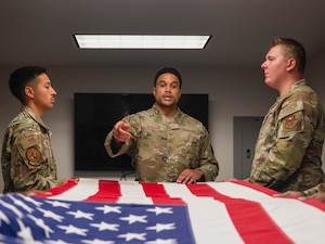 U.S. Air Force Tech. Sgt. Jacakori Burbank (center), Luke Honor Guard program manager, instructs Senior Airman Jesus Gerard (left), Luke Honor Guard guardsman, and Senior Airman Ian Crispen (right), Luke Honor Guard lead trainer, on flag-folding procedures, Aug. 14, 2025, at Luke Air Force Base, Arizona.