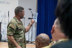 Col. Maxwell on the left of frame presents a brochure to a crowd