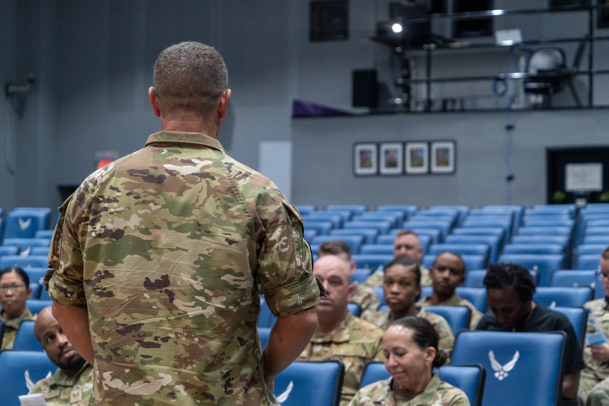 Col. Maxwell with back turned in the foreground, left of frame, speaks to a crowd in the background