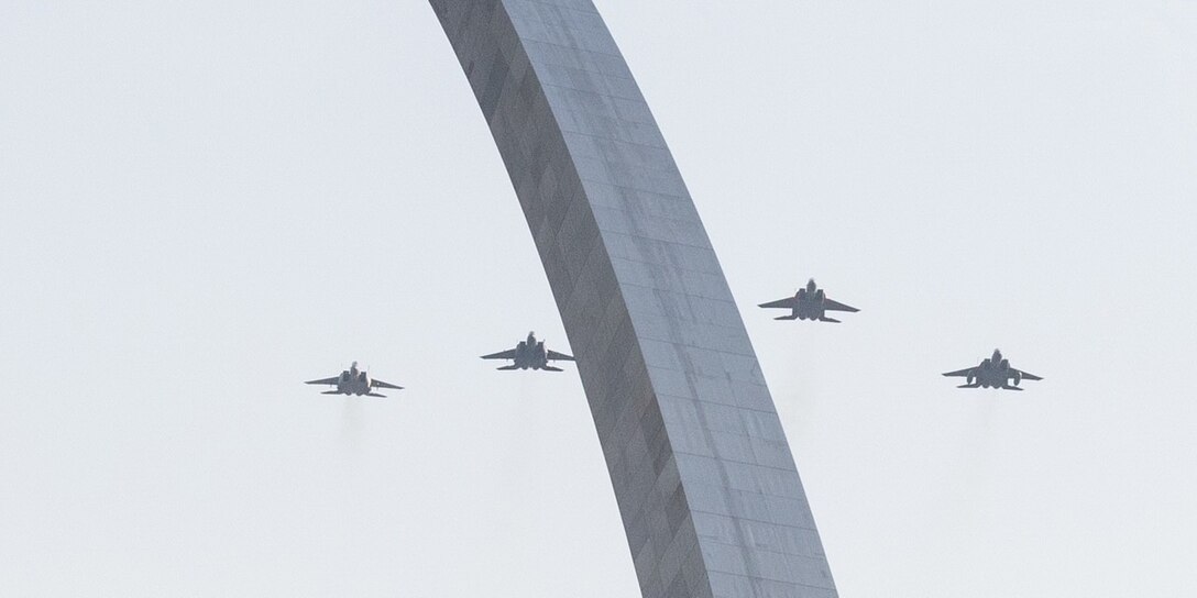 Four jets fly in the sky above an arch