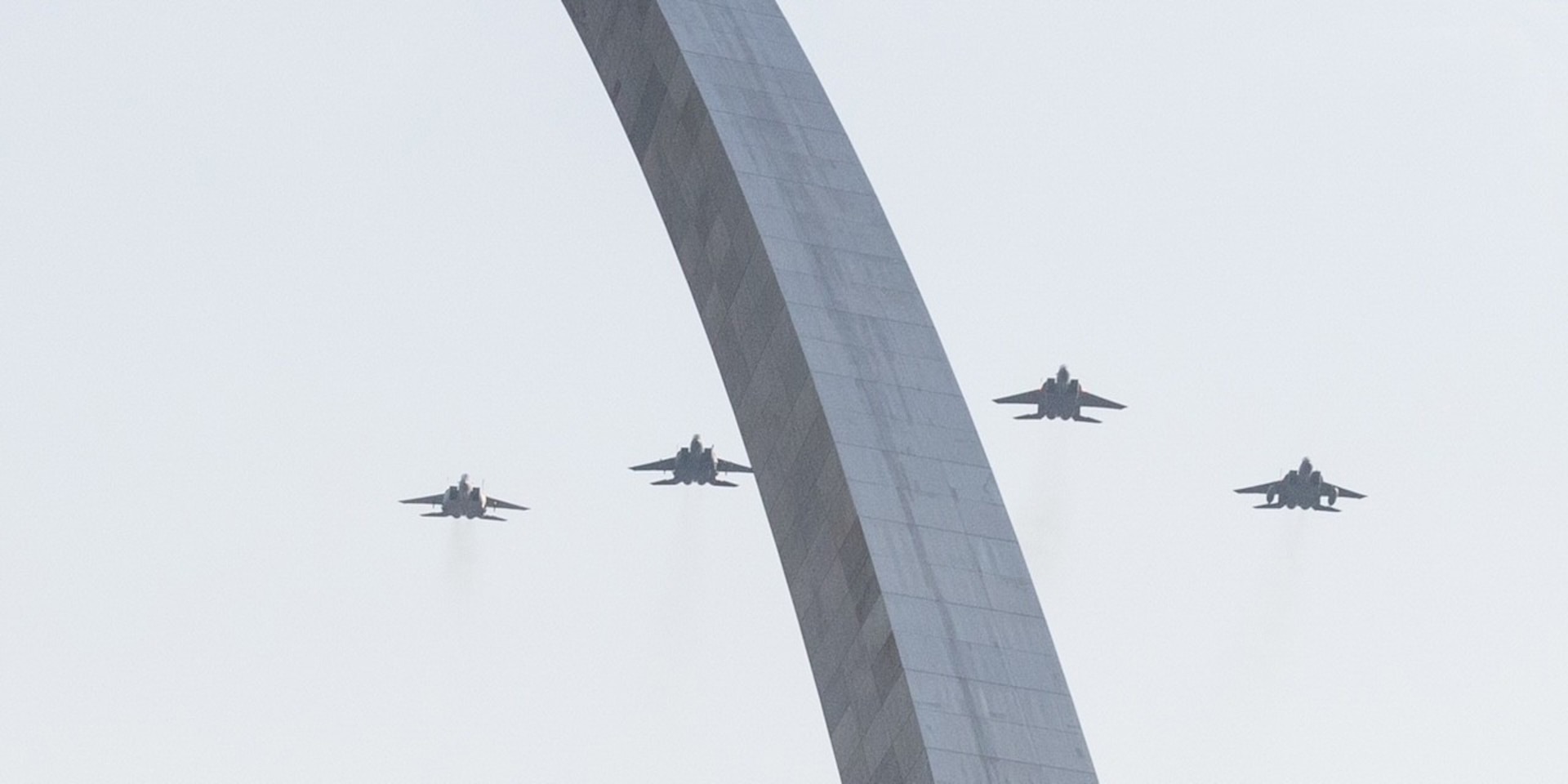 Four jets fly in the sky above an arch