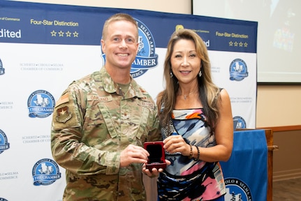 Commander in uniform holds coin box with president of the Chamber.