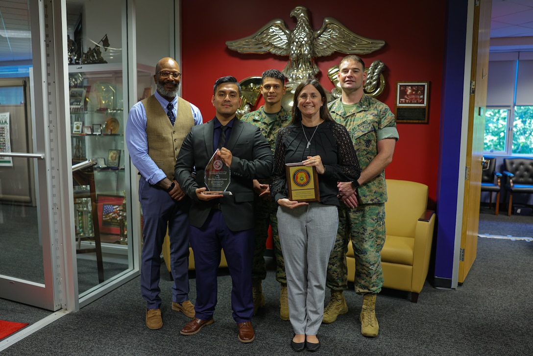 Treba Henderson, left, the deputy command inspector general, Diego Coral-Erazo, an investigative compliant assistant, Sgt. Roberto Morales, center, an investigative compliant specialist, Elizabeth Daniels, an investigative compliant specialist, and Lt. Col. Eric Spitznogle, right, the command inspector general, all members of the Marine Corps Recruiting Command inspector general section, pose with the General Shoup Superior Performance Award and Command Inspector General Superior Performance Award at MCRC Headquarters at Marine Corps Base Quantico, Virginia, Aug. 27, 2025. The inspector general team at MCRC demonstrated the highest levels of Marine Corps efficiency, integrity, and institutional readiness and set a high standard for other units to emulate through their performance during Fiscal Year 2024-25. (U.S. Marine Corps photo by Sgt. Aidan Hekker)