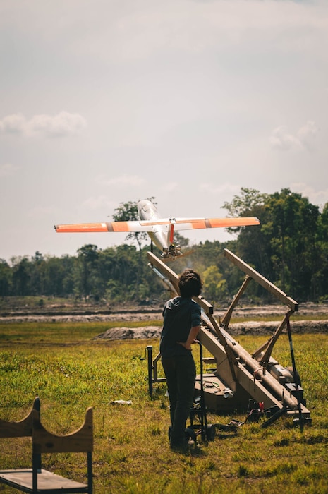 A man in civilian attire with his back to the camera launches a drone from a launching platform.