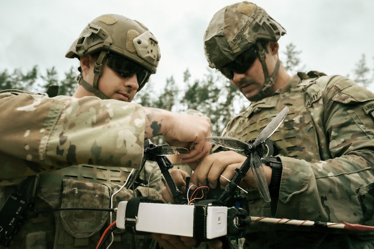 Two soldiers in camouflage military uniforms work on a drone.