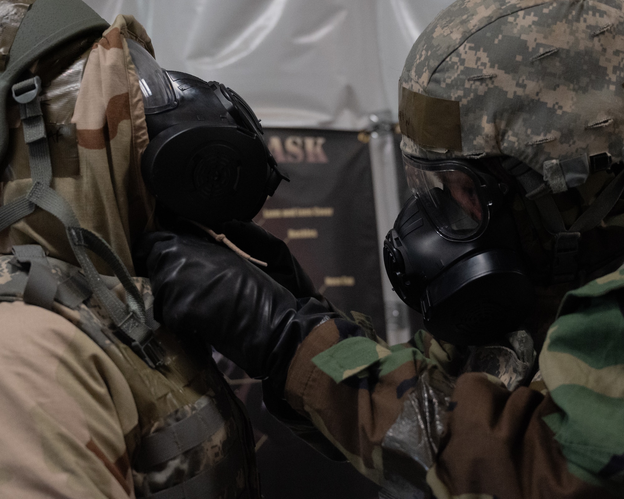 Two airmen face each other and put on each other's gas mask
