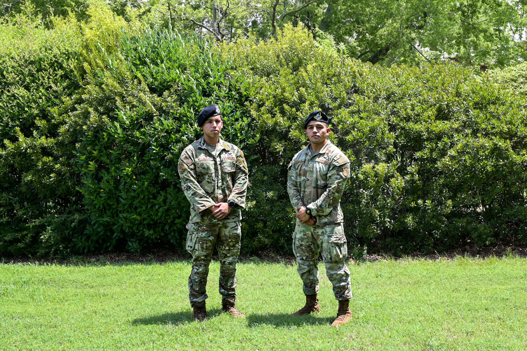 Two uniformed men stand on grass next to each other.