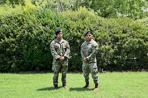 Two uniformed men stand on grass next to each other.