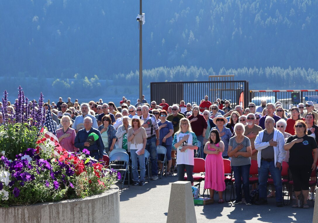 Attendees stand at attention while the U.S. National Anthem is played during Libby Dam's 50th commemoration, Aug. 23, 2025. Community band Big Sky Bows and Blowhards performed the National Anthem, while Montana Historian Mr. Rich (Ray) Aarstad read the names of the employees who lost their lives during the memorial unveiling.