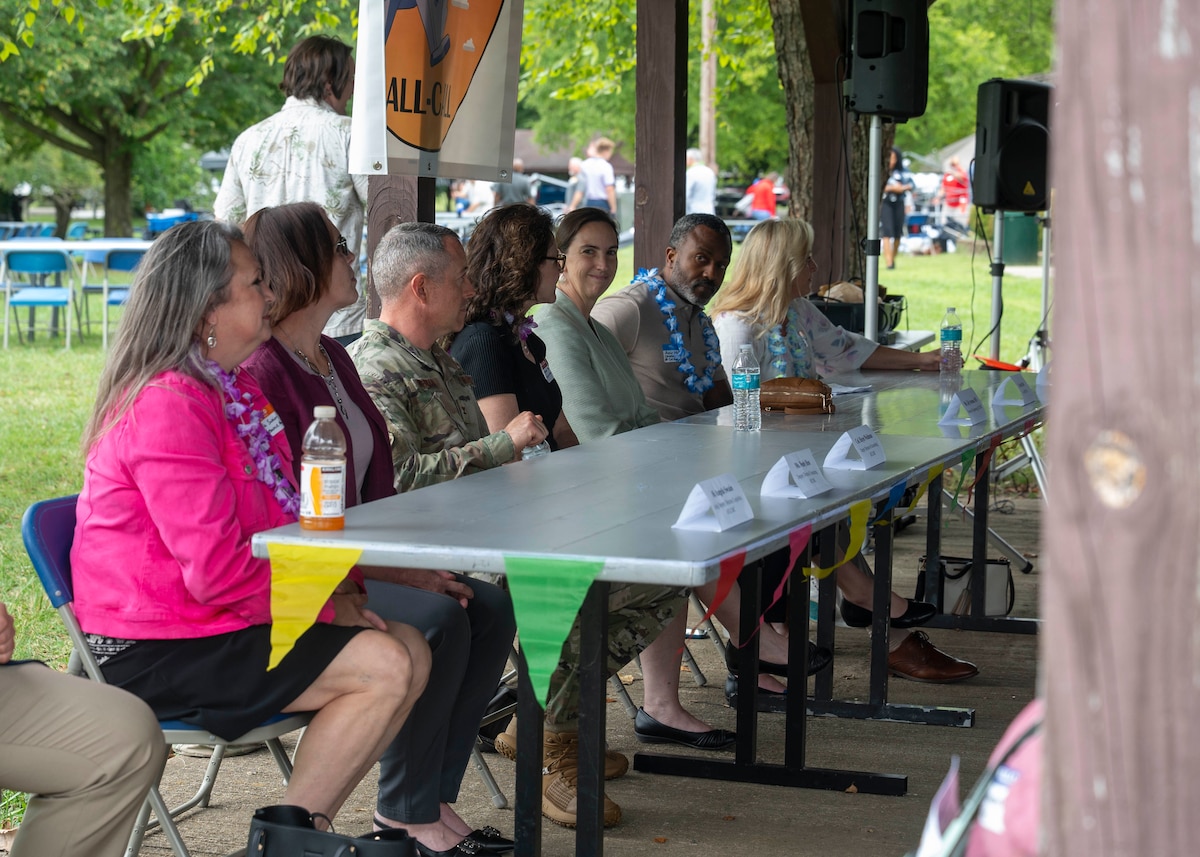 Individuals in business casual attire sit in a line at a table with name tents.