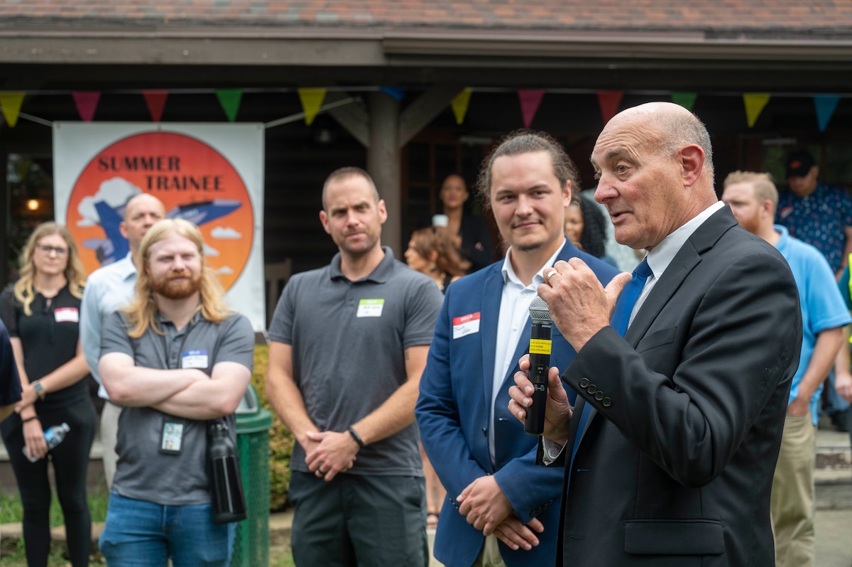Man in suit talks to younger employees while holding a mic.