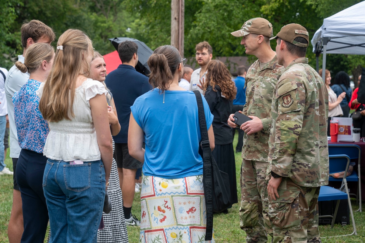 Individuals in summer clothes and Air Force fatigues stand outside, talking.