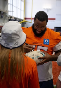 U.S. Air Force Airman First Class Christina P. Gein, 50th Force Support Squadron, Schriever Space Force Base, receives an autograph from a Denver Broncos player during the USAA Salute to Service Boot Camp, at Broncos Park, Englewood, Colorado, August 21, 2025. During the boot camp, service members from multiple installations were invited to observe a Broncos practice and meet the players. (U.S. Space Force photo by Ethan Johnson)