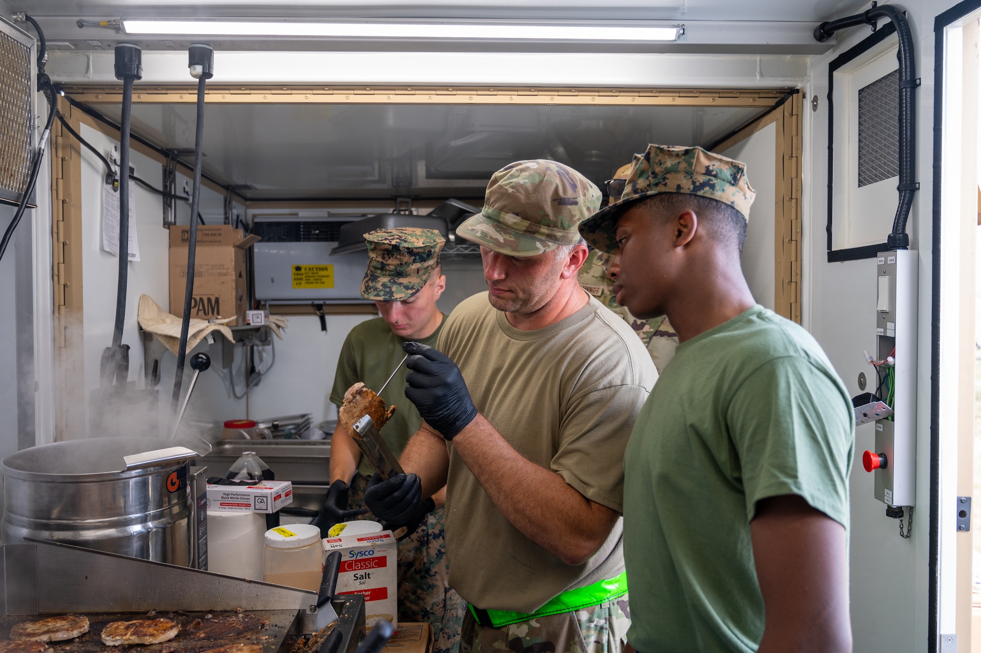 U.S. Air National Guard Tech. Sgt. Clint Vose, a kitchen production lead, 131st Bomb Wing, shows U.S. Marine Corps Lance Cpl. Wyatt Bressler (left) and Lance Cpl. Kwadir Young (right) with Bulk Fuel Company Bravo, 6th Engineer Support Battalion how to monitor for food safety at Exercise Northern Strike 25-2, Aug. 6, 2025, Oscoda, Michigan. Joint efforts between the two branches during the exercise were conducted in an expeditionary kitchen in preparation for real-world operations in deployed settings. (U.S. Air National Guard photo by Senior Airman Grace Bynum)