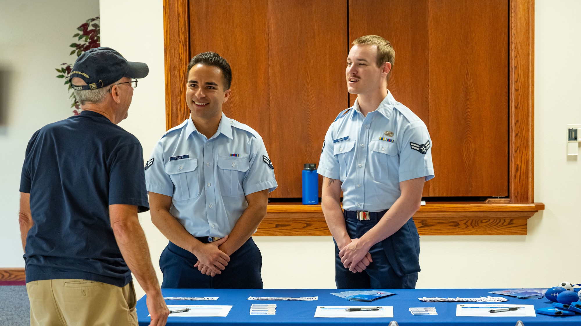Airman 1st Class Vincent Padilla & Wesley Davies, 5th Bomb Wing public affairs specialists, welcome a member of the Minot community during the Sentinel program town hall in Minot, North Dakota, Aug. 26, 2025. The activity educated residents, civic leaders, and local workforce members regarding major features of the Sentinel program, such as future developments, economic benefits, infrastructure construction, and environmental investigations.