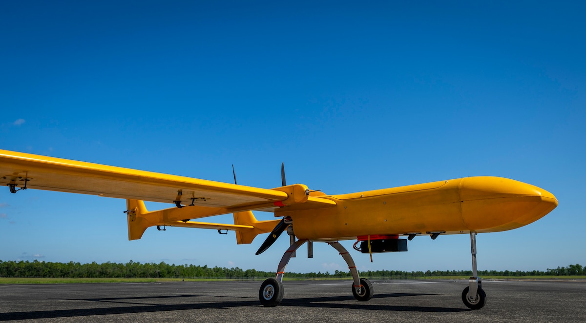 A bright orange unmanned aircraft sits on a tarmac with its wheels down.
