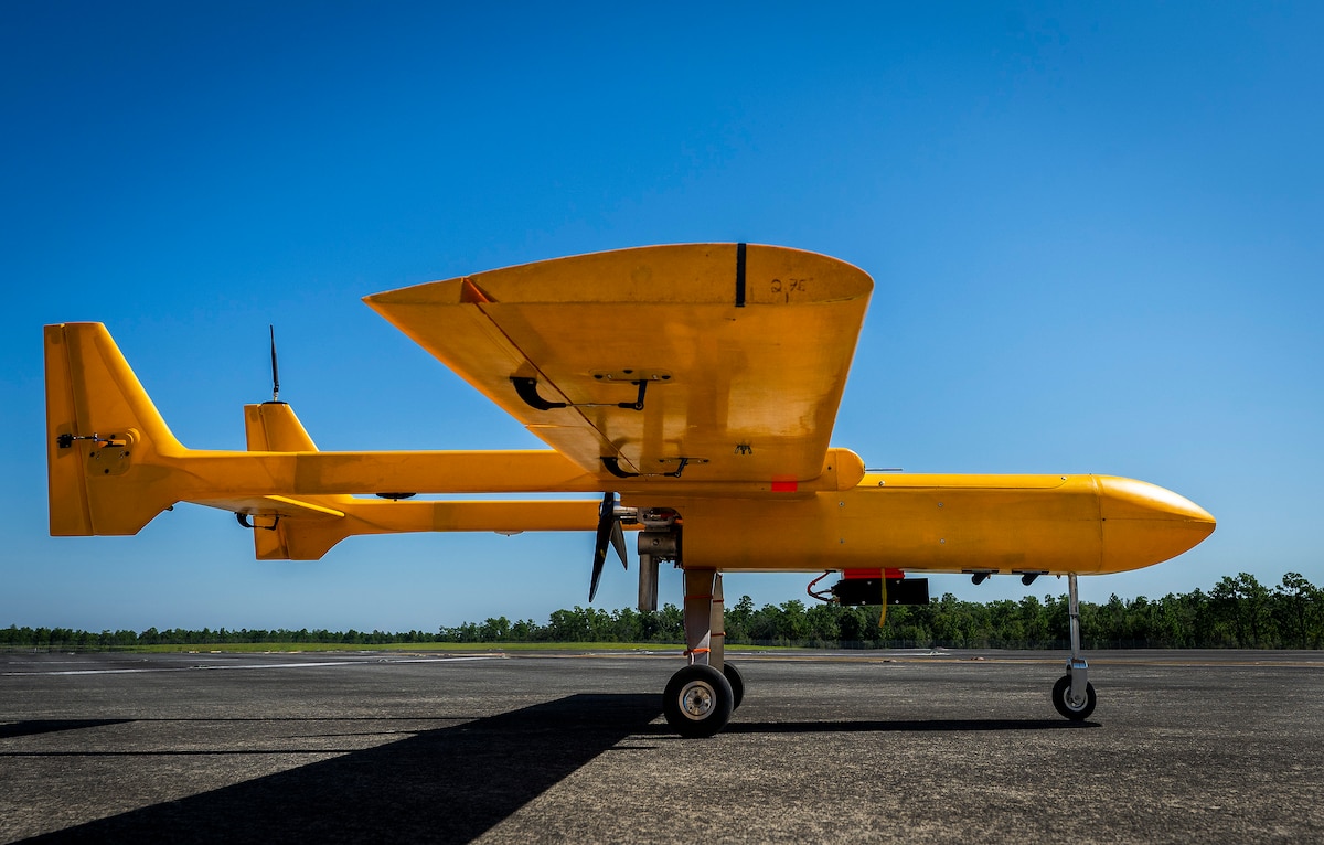 A bright orange unmanned aircraft sits on a tarmac with its wheels down.