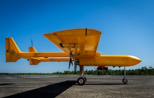 A bright orange unmanned aircraft sits on a tarmac with its wheels down.