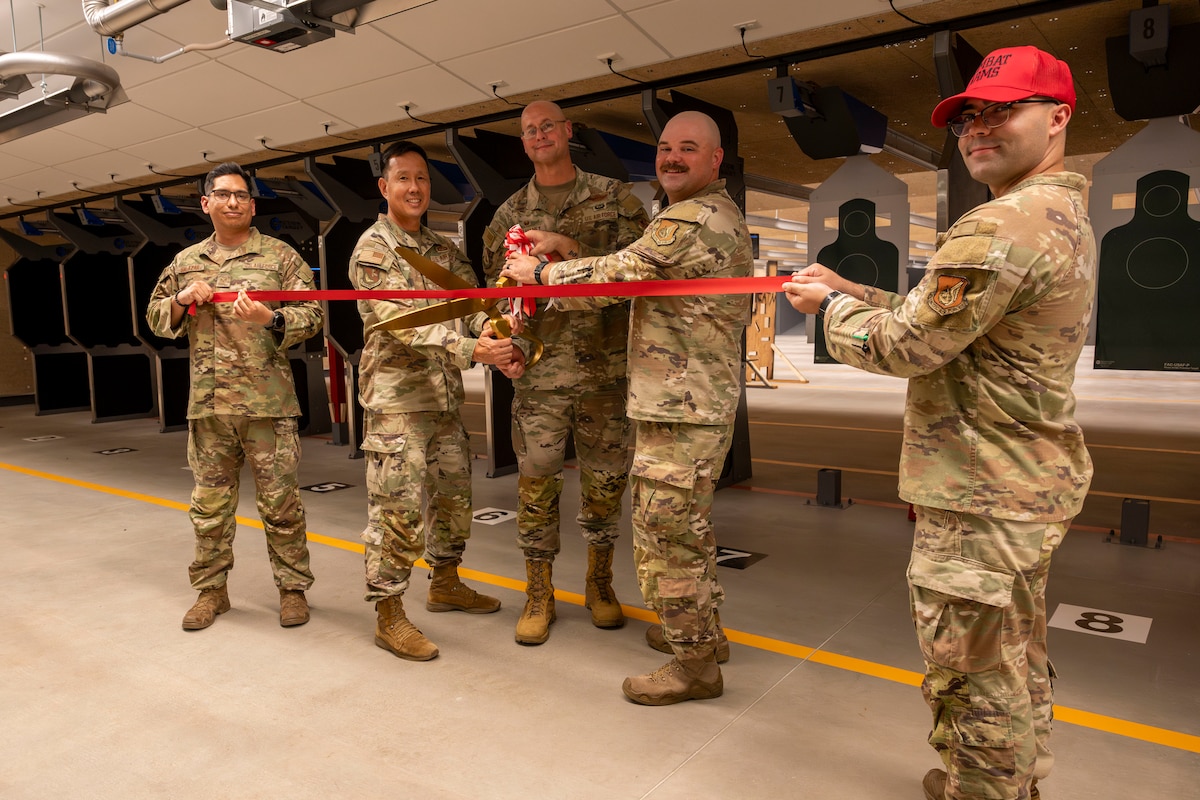 Military members pose for a photo as they hold a ribbon and large scissors.