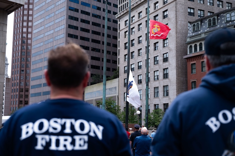 Boston fire fighters stand and watch as flags are raised during the opening ceremony hosted by U.S. Marines with the Special Purpose Marine Air-Ground Task Force-250 at the City Hall Plaza during Marine Week Boston, Aug. 21, 2025. As the Marine Corps marks its 250th year, Marines worldwide observe this historic milestone, paying tribute to generations of valor, duty, and the enduring spirit of Semper Fidelis. (U.S. Marine Corps photo by Lance Cpl. Matthew A. McDonnell)