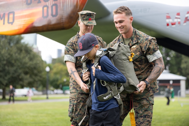 U.S. Marine Corps Sgt. Cody Miller, a native of Helena, Montana, and an airborne and air delivery specialist with Special Purpose Marine Air-Ground Task Force-250, assists an event attendee to put on a parachute during Marine Week Boston, Aug. 21, 2025. Marines stationed across the globe commemorate the 250th anniversary of the Marine Corps, honoring a distinguished legacy of service, sacrifice, and unwavering fidelity to both the nation and fellow Marines. (U.S. Marine Corps photo by Sgt. Matthew Romonoyske-Bean)
