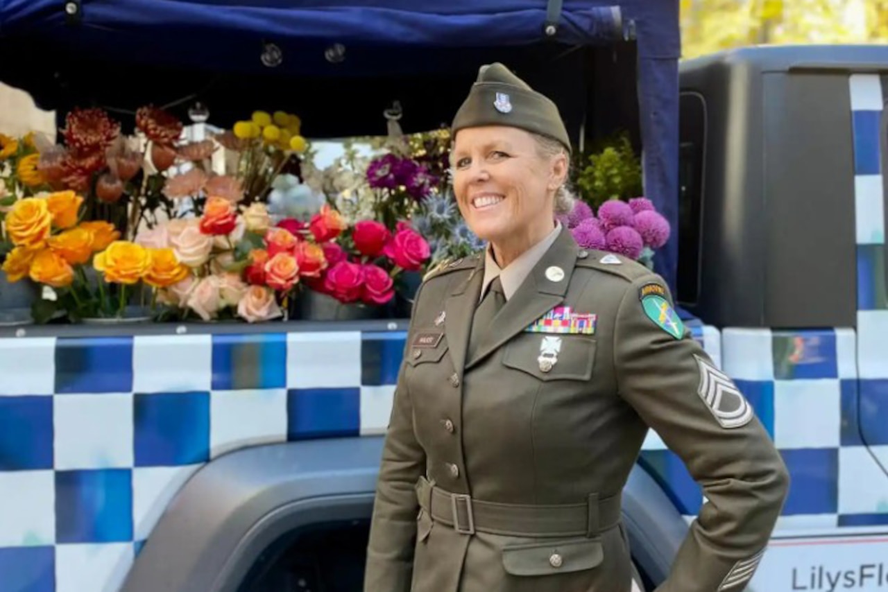 A soldier poses in front of a flower bouquet cart outside on a sunny day.