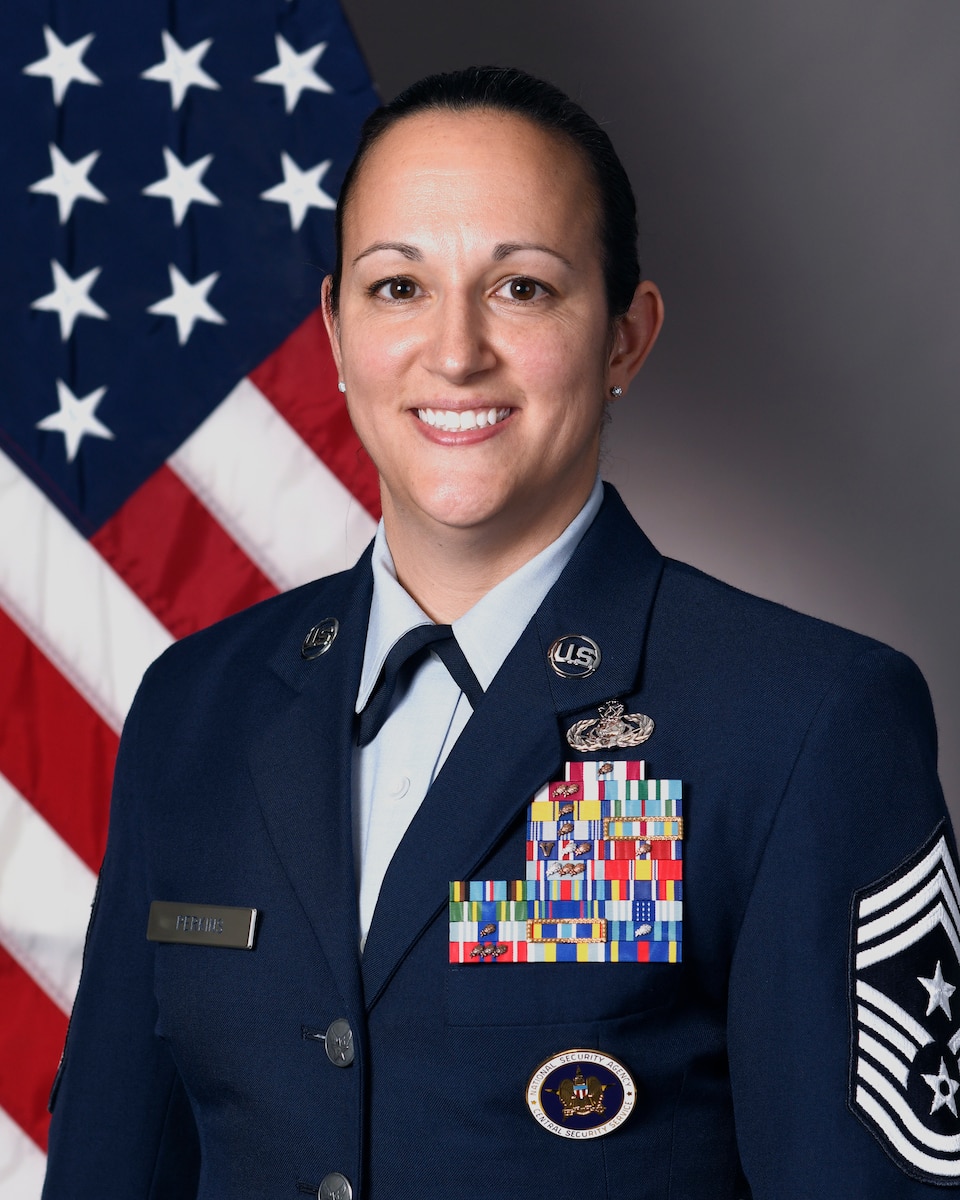 Airmen in dress uniform sitting in front of flag