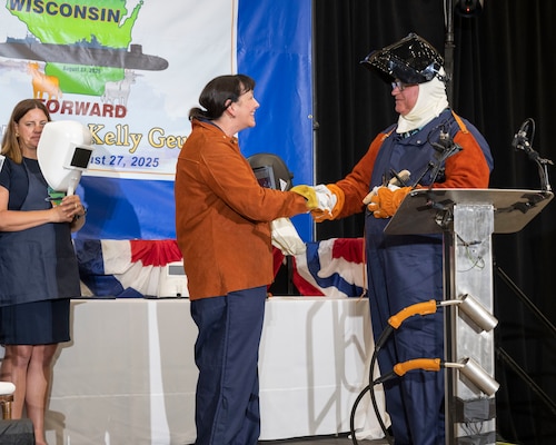 Dr. Kelly Geurts, ship sponsor of the future Columbia-class ballistic missile submarine USS Wisconsin (SSBN 827), left, shakes hands with Robert Ray Jr. after welding her initials in the keel of the ship during the ship’s keel-laying ceremony.