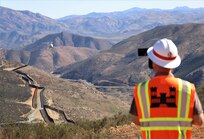 a man in a reflective vest and hard hat takes a video shot looking down a long length of new border barrier
