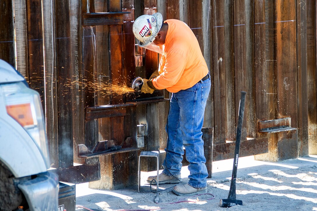 A man in protective gear cuts metal along the border barrier fencing.