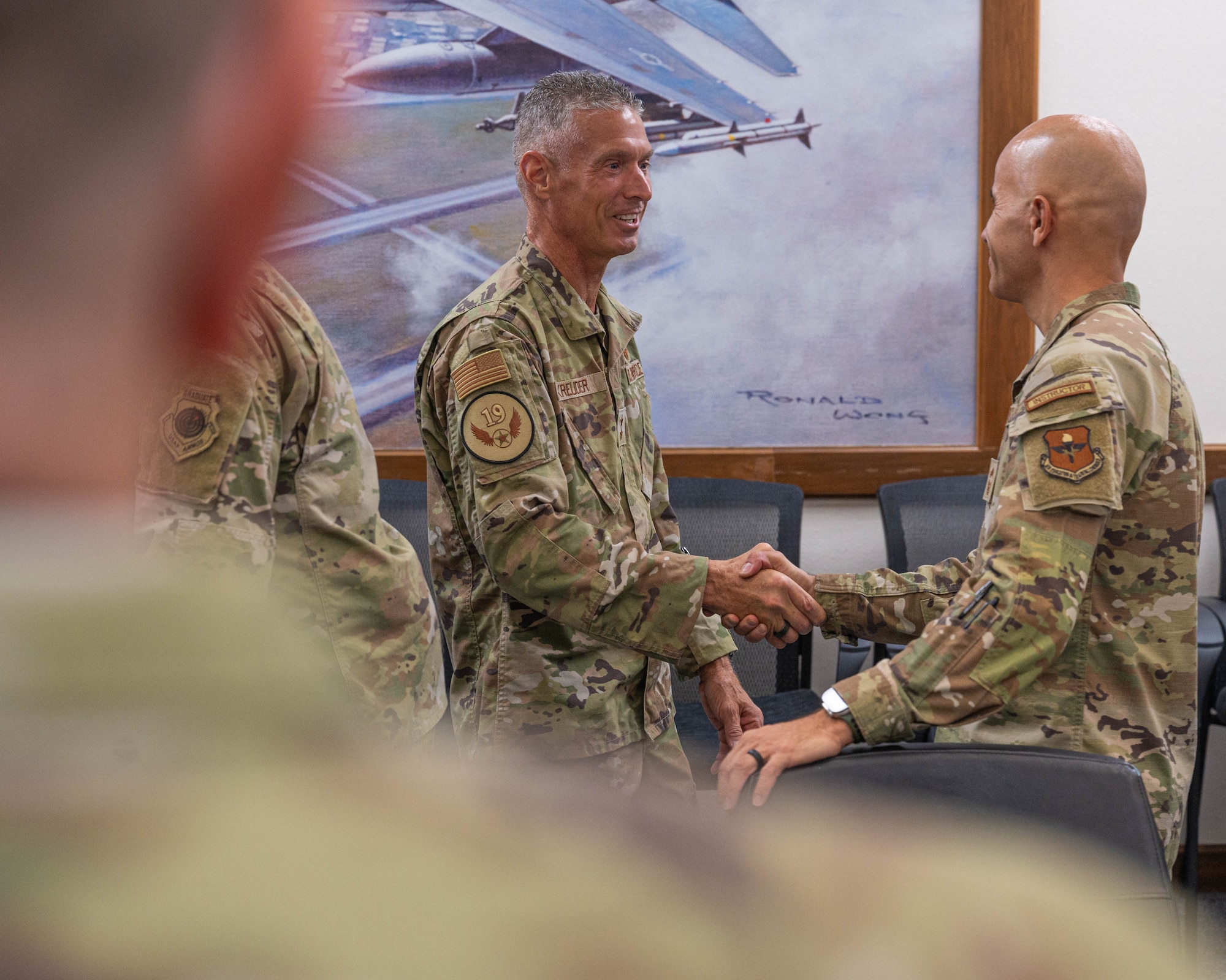 U.S. Air Force Maj. Gen. Gregory Kreuder, 19th Air Force commander, and Chief Master Sgt. Jose Negron, 56th Maintenance Group senior enlisted leader, shake hands in the headquarters conference room