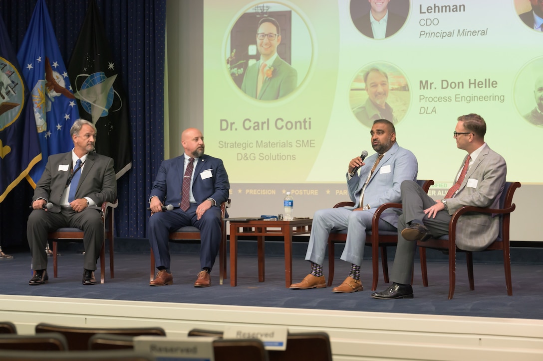 Men sitting in a row on stage for panel discussion.