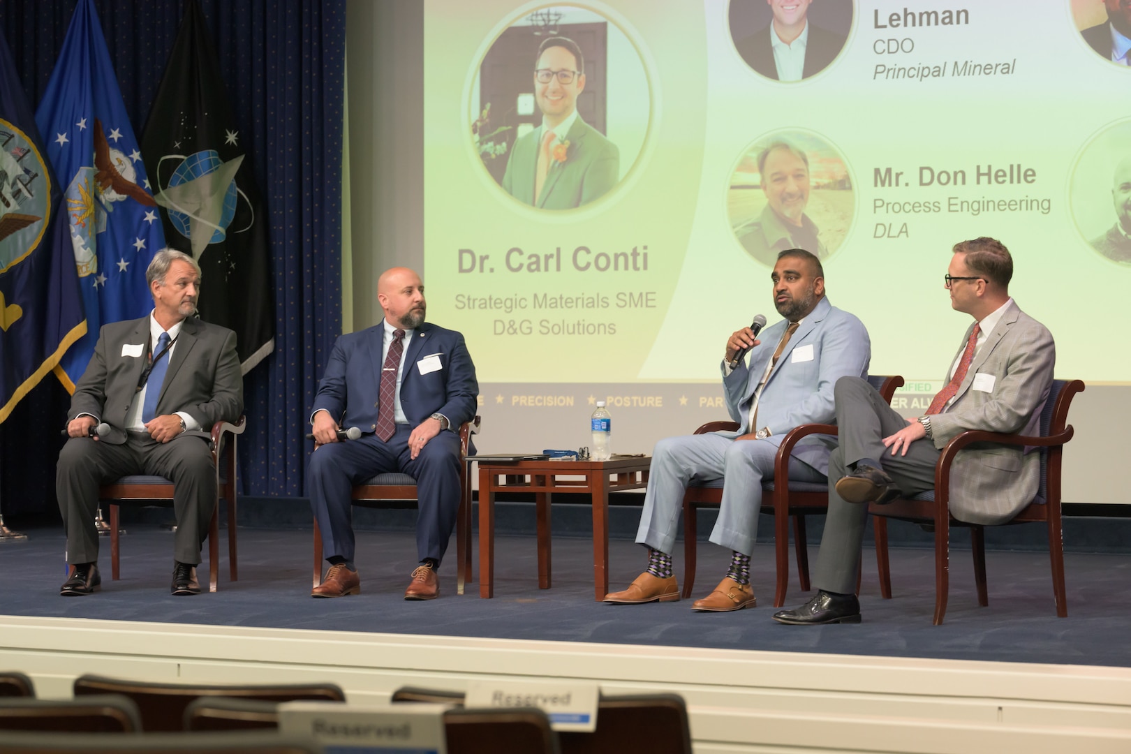 Men sitting in a row on stage for panel discussion.