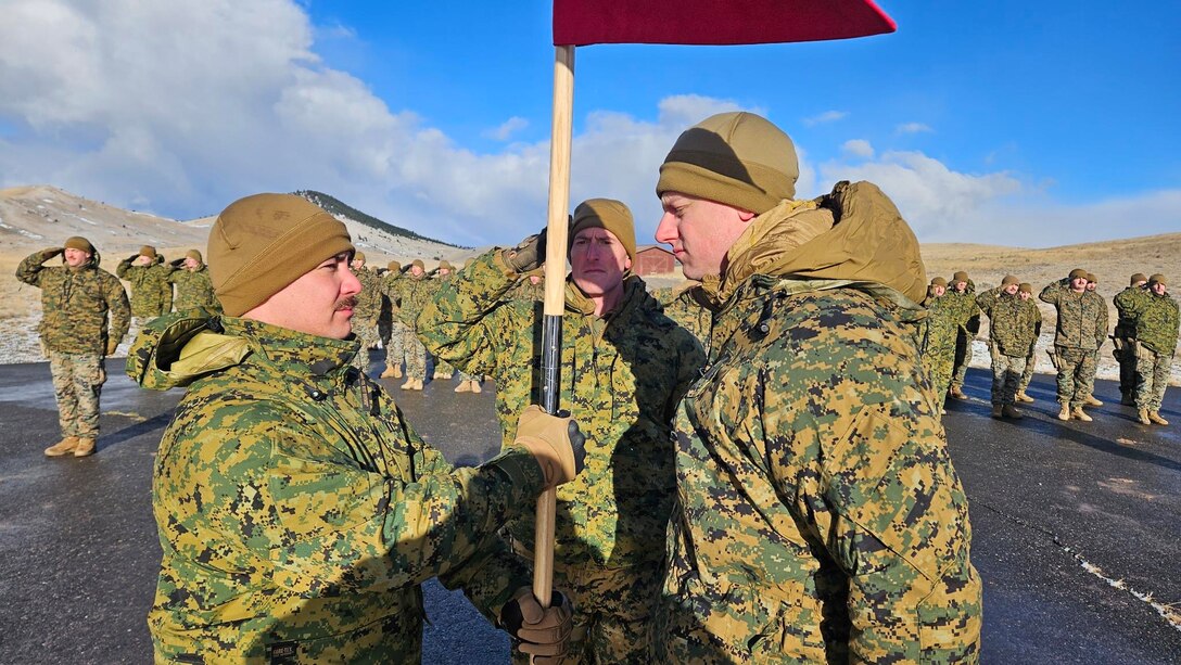 U.S. Marine Corps Capt. Avery Moore, outgoing commanding officer, 4th Law Enforcement Battalion, Force Headquarters Group, Marine Forces Reserve, passes the guidon to Capt. Garrett Gundy, incoming commanding officer, symbolizing the passing of command during a change of command ceremony at Ft. Harrison, Helena, Montana, March 20, 2025. The change of command ceremony represents the official passing of authority from the outgoing commander to the incoming commander. (U.S. Marine Corps photo by courtesy of 4th Law Enforcement Battalion)