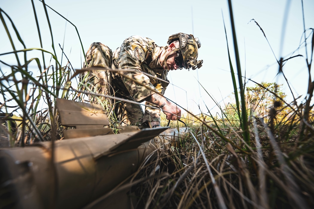 A man in uniform stands over a simulated explosive.