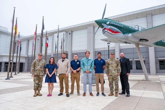 A group of people lined up stand together for a photo outside of a building.