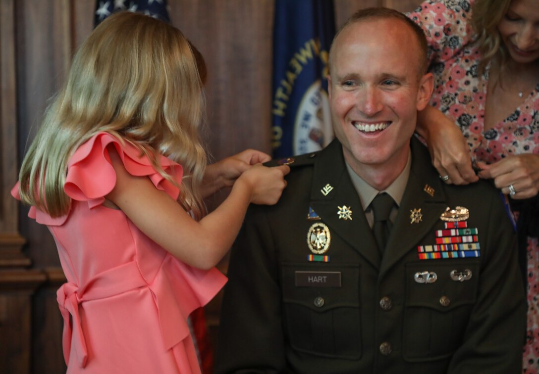 U.S. Army Col. Derek Hart's daughter, Helen and wife, Emily(top corner), pin on his new rank to his uniform during his promotion ceremony at the Louisville Country Club in Louisville, Kentucky, Aug. 20, 2025