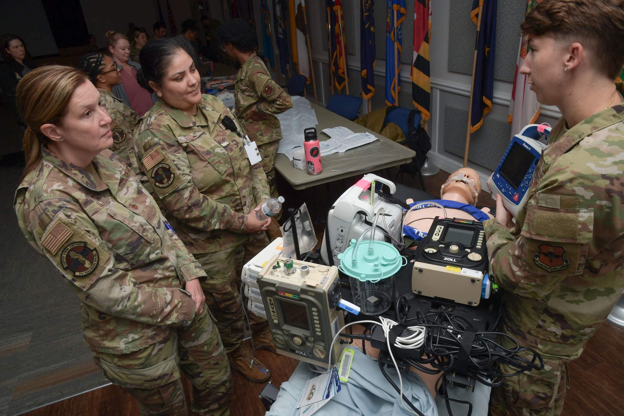 A group of women stand around a mannequin with expeditionary medical equipment on display.