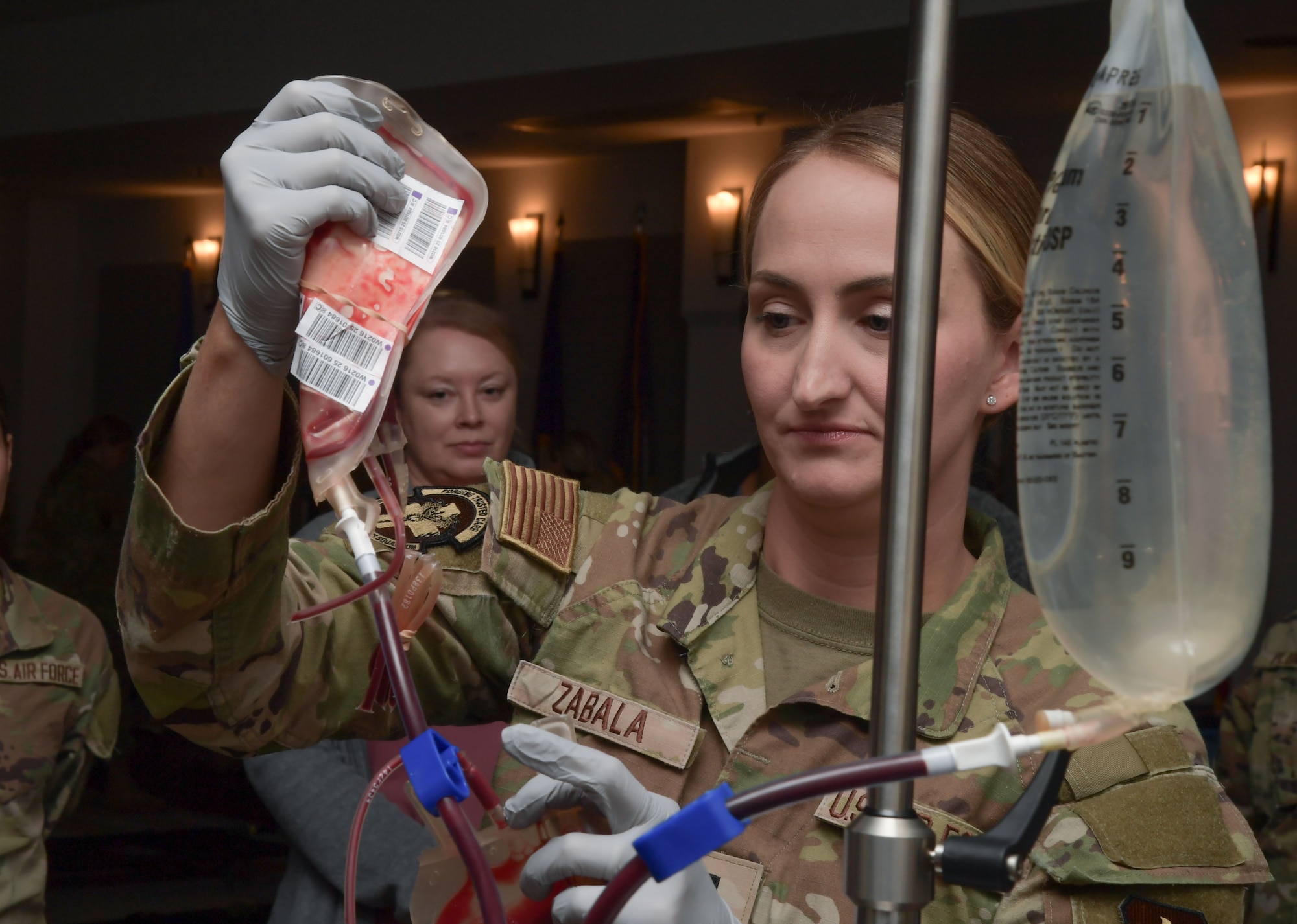 A woman in military uniform hangs an IV bag.