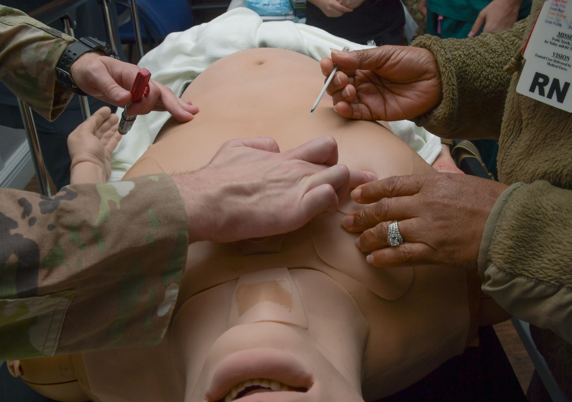 A pair of hands work together to insert a needle into a mannequin's chest.
