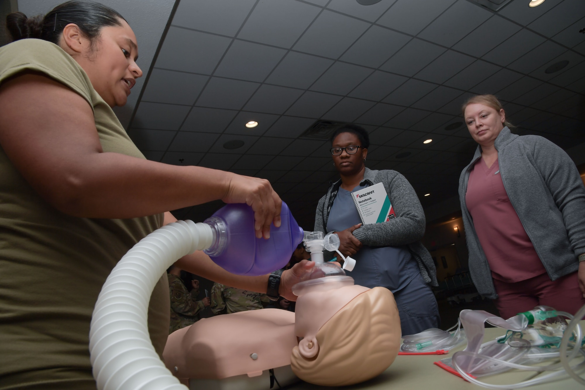A woman holds a respiratory demonstration on a mannequin while two ladies watch.