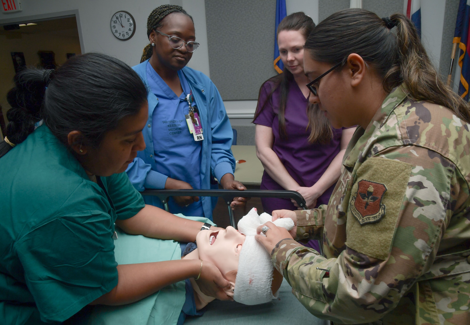 Two ladies wrap a gauze around a mannequin's head while two other ladies watch.