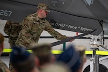 An Airman reveals the name of a general on the side of an F-35 in front of a crowd of people at a ceremony.